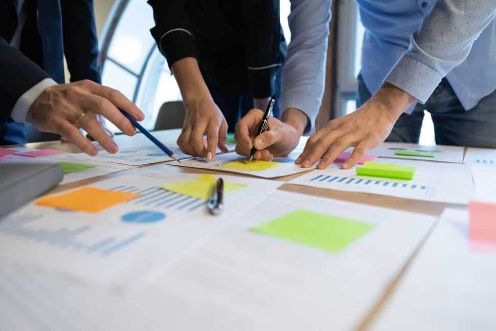 Group of people collaborating with colorful sticky notes and documents in a formal workspace for beMarketing.